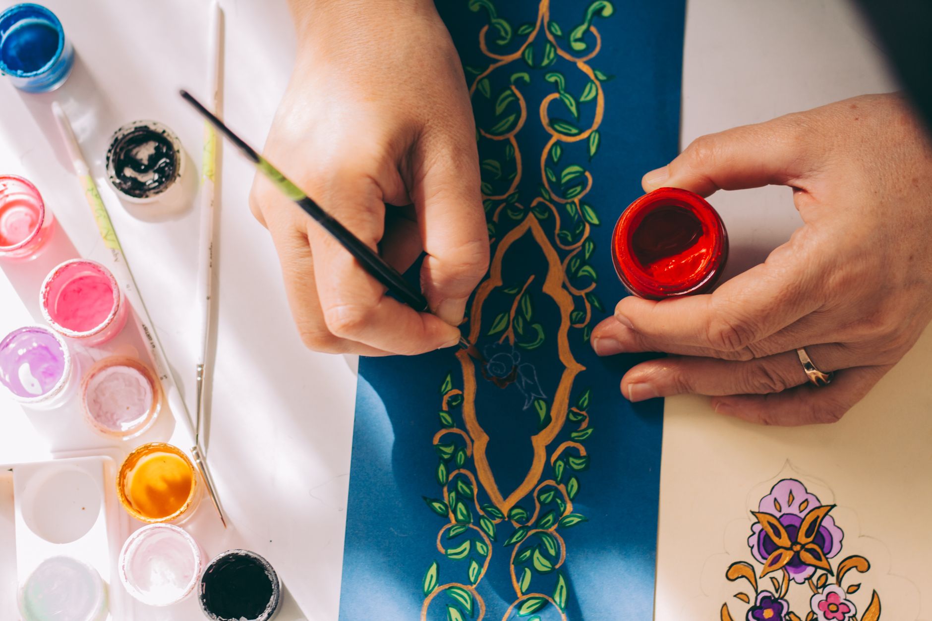 Hands painting a colorful pattern with red paint and brushes on paper, highlighting artistic creativity in Carlsbad, CA